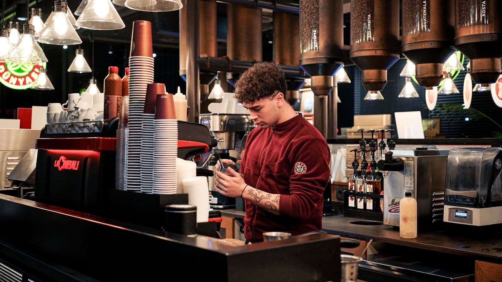 Barista przy ekspresie w kawiarni, ciepłe światło nad ciemnym barem