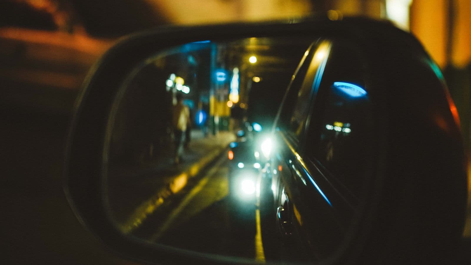 Nocna ulica z reflektorami aut odbita w bocznym lusterku samochodu
