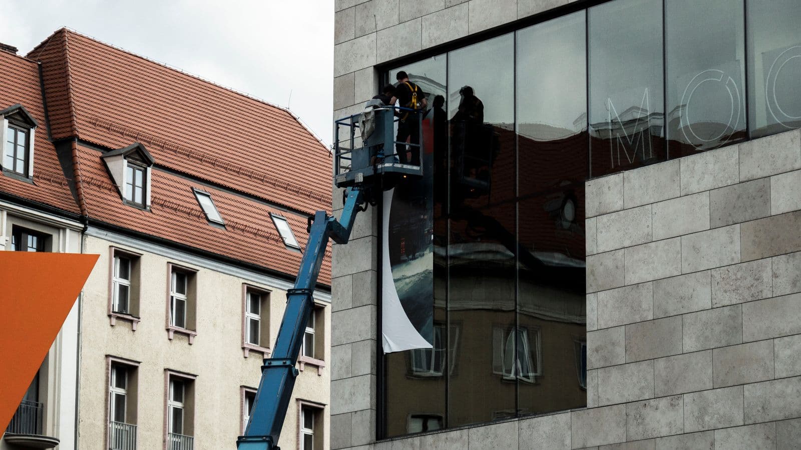 Ekipa na podnośniku montuje wielkoformatowy baner na przeszklonej elewacji