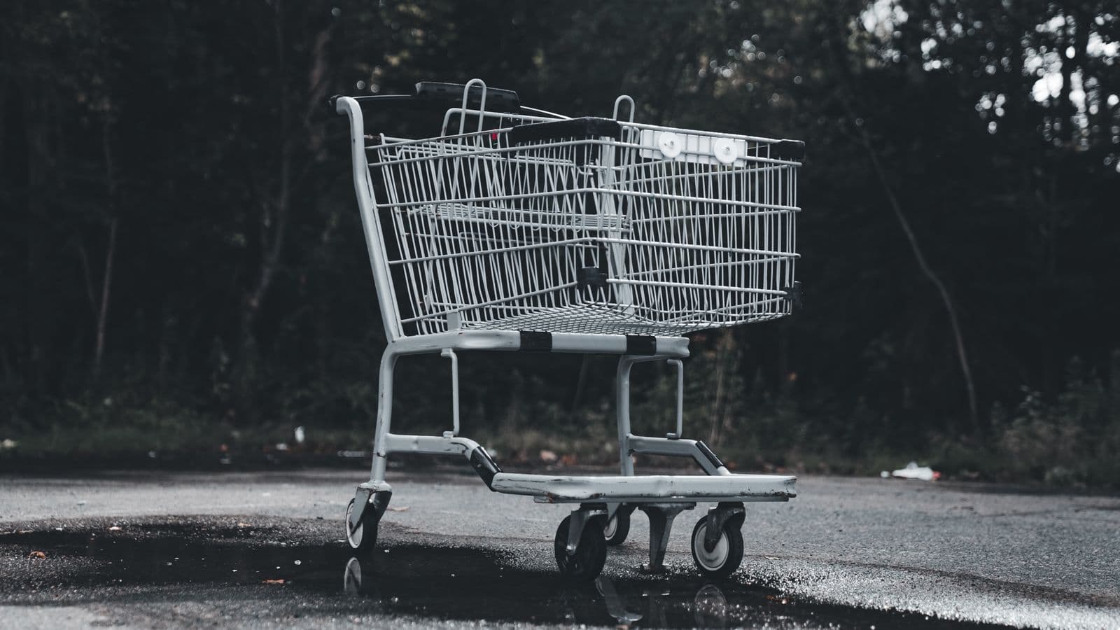 Porzucony wózek sklepowy na pustym parkingu, odbicie w mokrym asfalcie