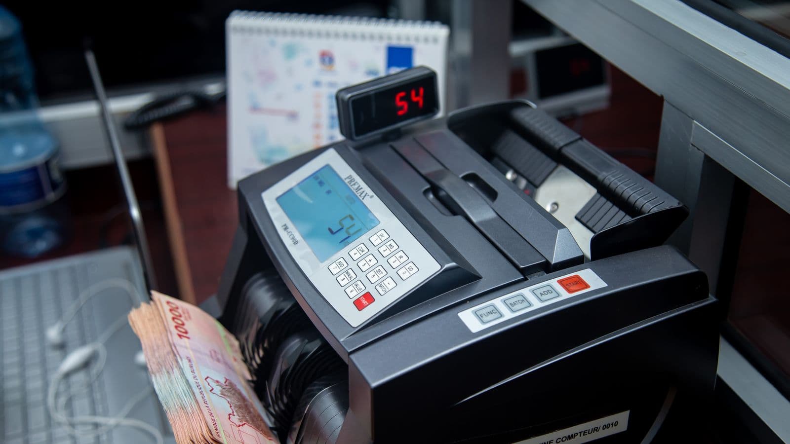 Maszyna licząca banknoty na biurowym blacie, plik pieniędzy w szczelinie